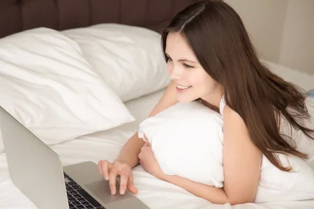Femme détendue utilisant son ordinateur confortablement installée dans son lit