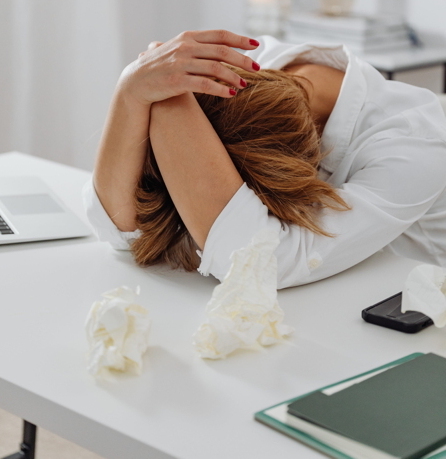 Femme stressée tenant sa tête dans ses mains à son bureau – Anxiété au travail accompagnement Perpignan
